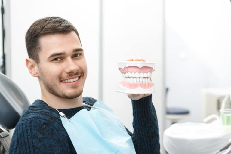 Cheerful,Young,Handsome,Man,Smiling,Holding,Dentures,Sitting,In,A